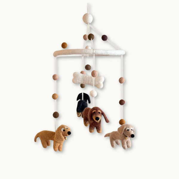 Handcrafted felt baby mobile featuring four Dachshund dogs, a felt bone, and coordinating neutral-toned felt balls suspended from a white circular frame.