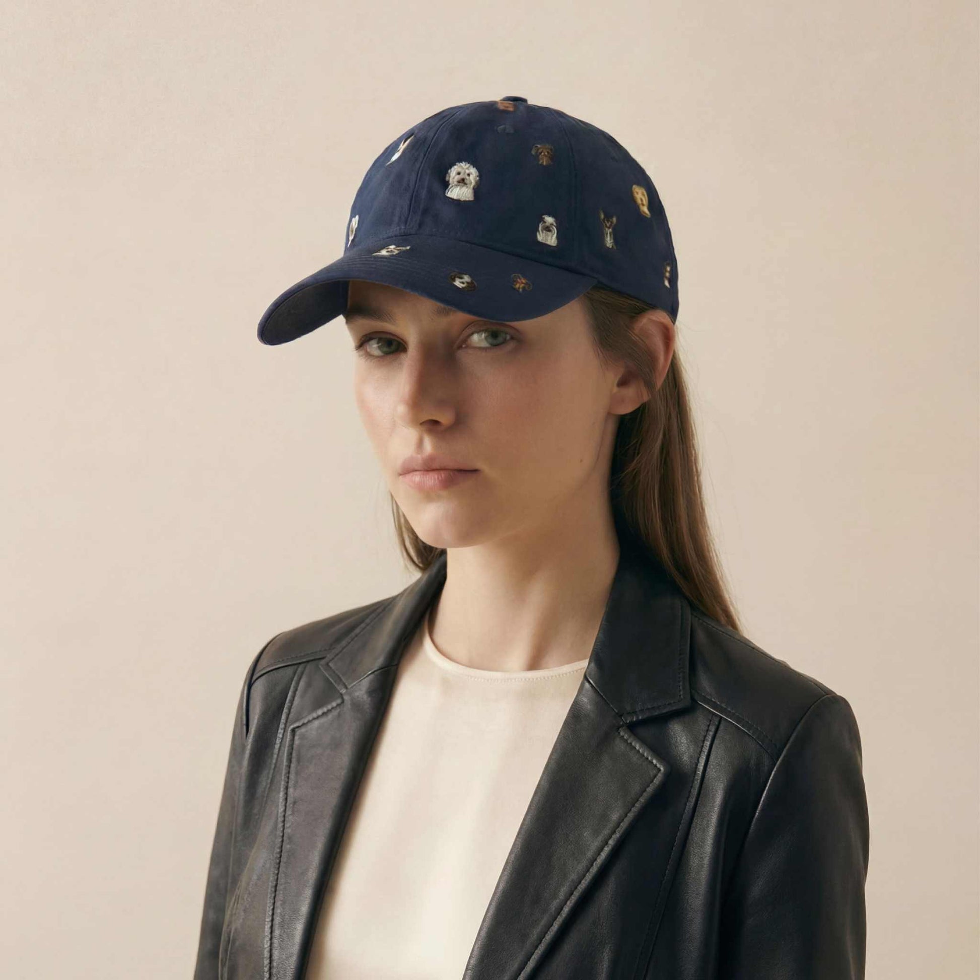 Woman wearing a navy cap with embroidered designs on a beige background