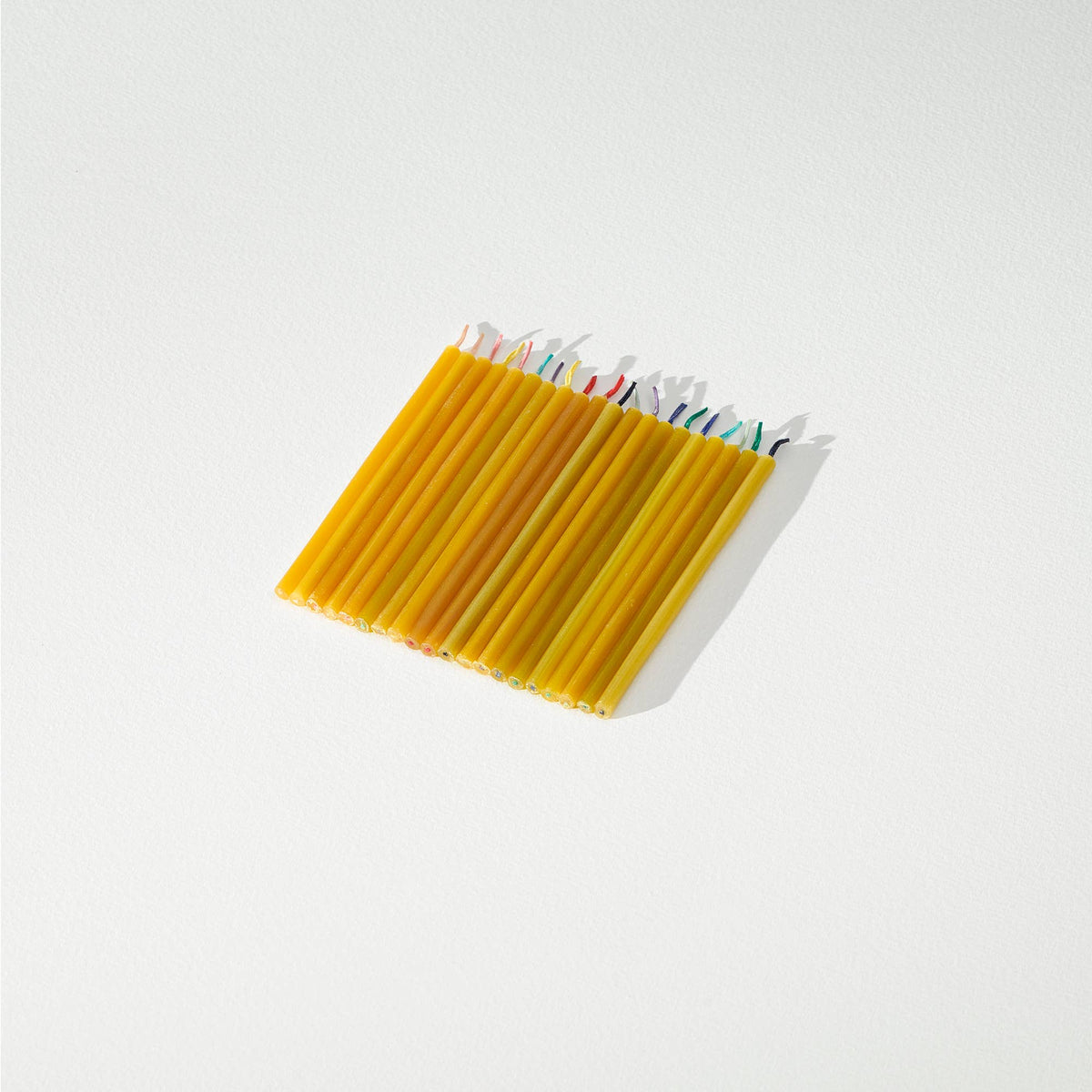 Set of 20 beeswax candles with colorful tips on a light background.