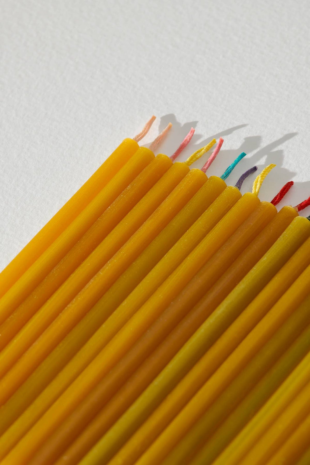 Beeswax candles with colored wicks on a light background.