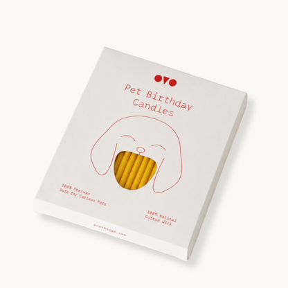 A boxed candle product labeled 'Pet Birthday Candles' shown at an angle on a clean white background. The package is white with a simple red line drawing of a dog face and red text, with a clear window revealing beeswax candles inside.