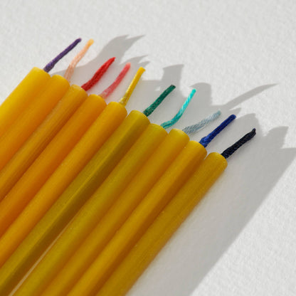 Slim beeswax candles with colorful wicks on a light background.