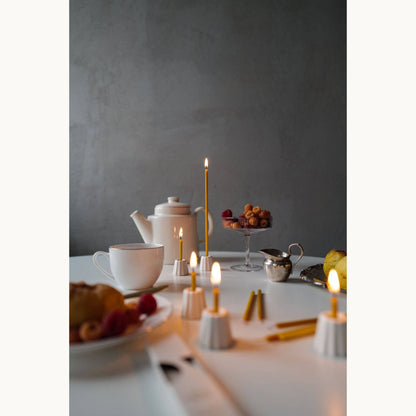 Tea set with slim beeswax candles and pastries on a table against a gray wall.