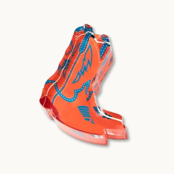 Bright orange cowboy boots napkin weight with blue western-style graphic patterns and white stitching details.