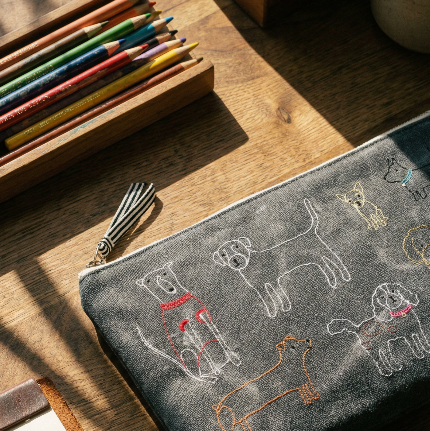 Gray pouch with dog illustrations on a wooden surface with colored pencils.