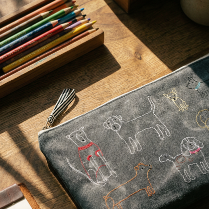 Gray pouch with dog illustrations on a wooden surface with colored pencils.