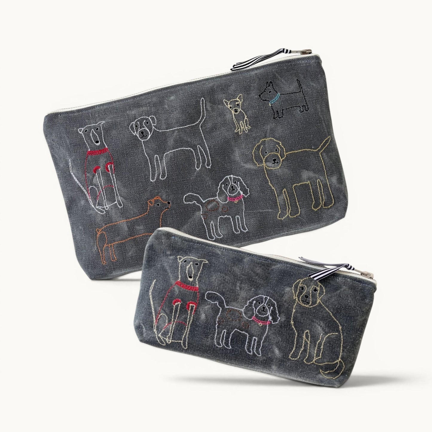 Two dark gray zippered pouches with embroidered dog illustrations, displayed on a clean off-white background.