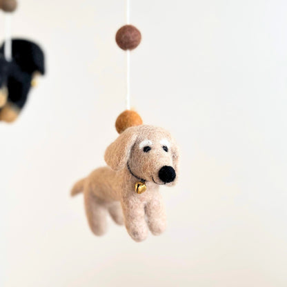 A felt dog mobile ornament hanging from a white string with wooden beads, shown against a soft white background.