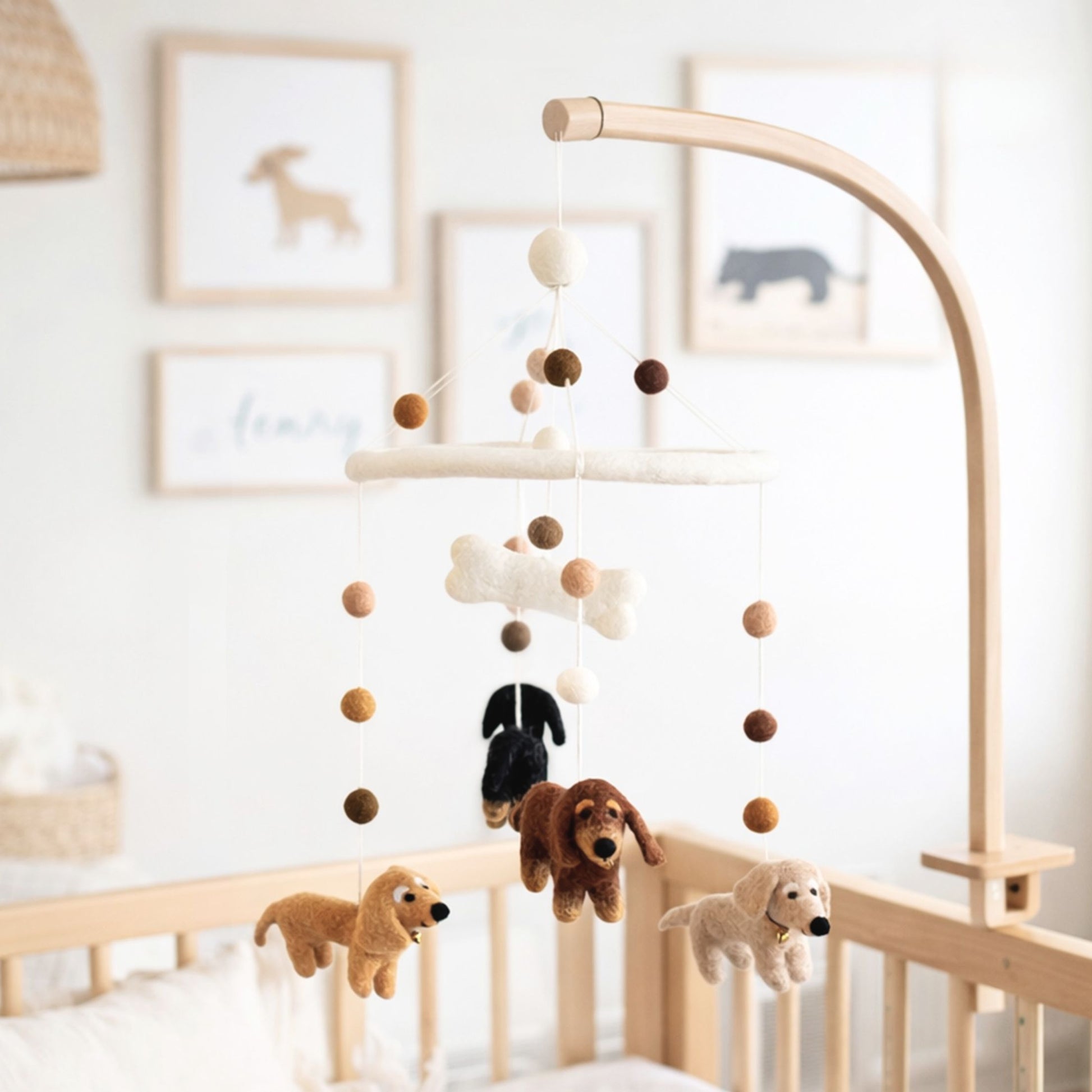 Handcrafted felt baby mobile featuring four Dachshund dogs, a felt bone, and coordinating neutral-toned felt balls hanging over a wooden crib.