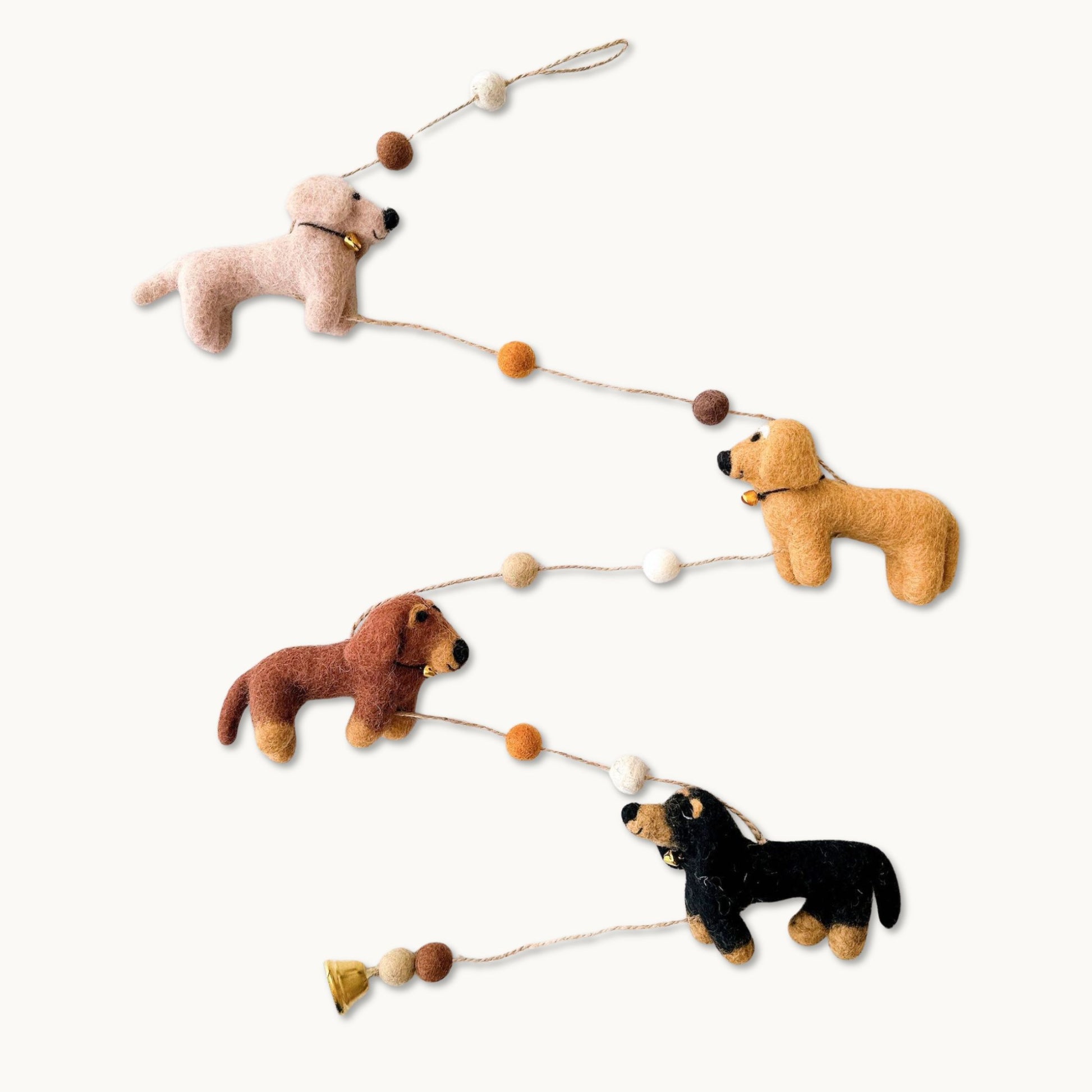 A felt dog garland featuring four different dog figures in cream, khaki, brown, and black, connected by a string with decorative wooden beads and a small bell.