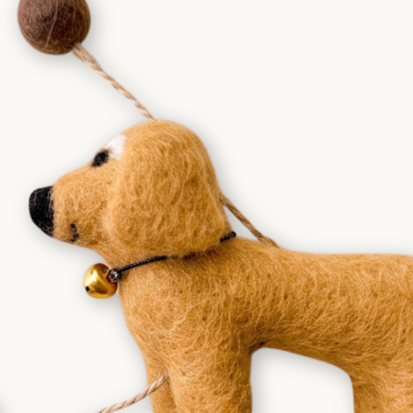 A felted wool dog in khaki color with a neutral string and felt brown ball, as part of a felt dachshund garland.