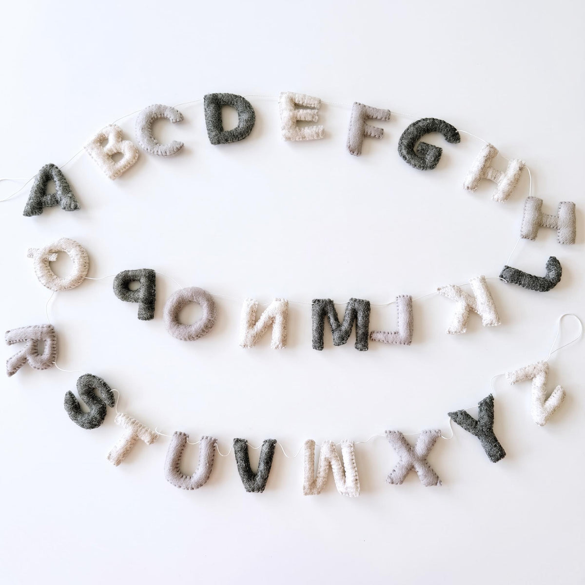 Grey-toned felt alphabet garland displayed on a white background.