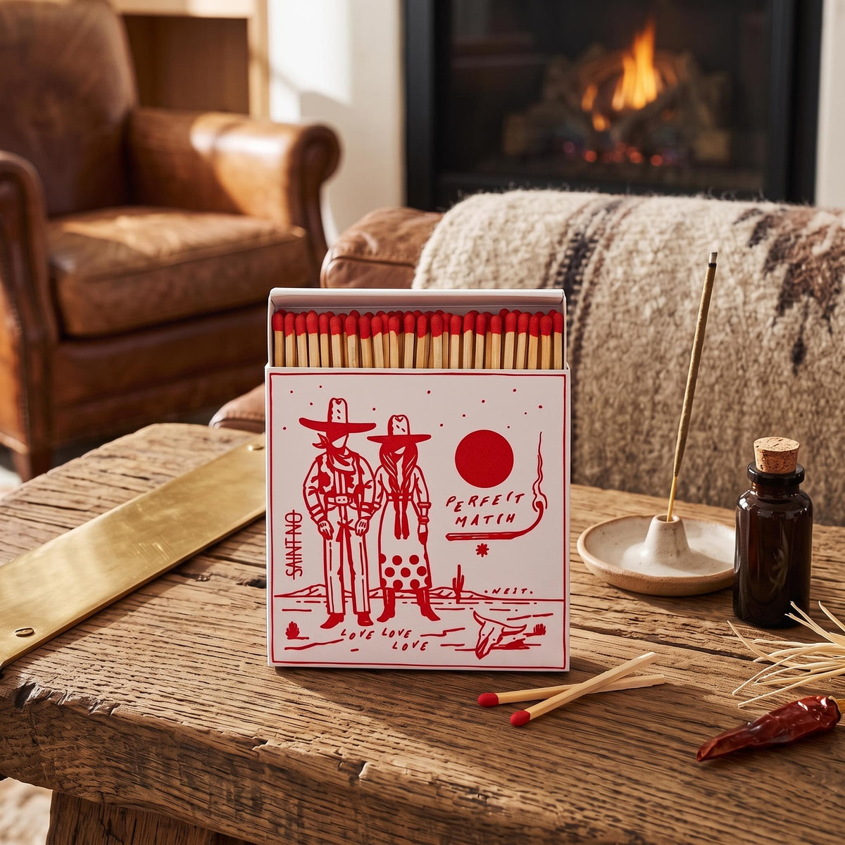 Matchbox with illustration of two people in cowboy hats and the text 'Perfect Match'., on a woodent table next to incense and a leather couch. Saint No, Archivist.