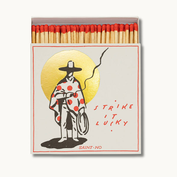 Matches box with illustration of person in polka dot coat and hat, text 'Strike it lucky', and brand 'Saint No'.
