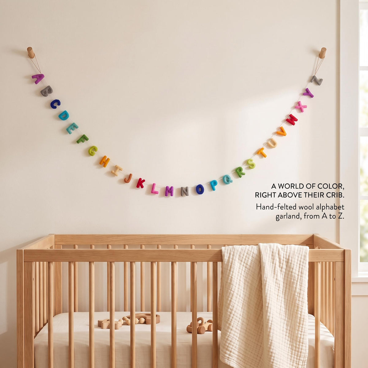 Colorful felt alphabet garland displayed in a neutral children's room over a crib.