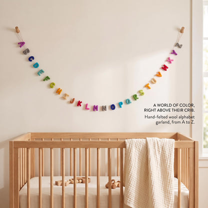Colorful felt alphabet garland displayed in a neutral children's room over a crib.