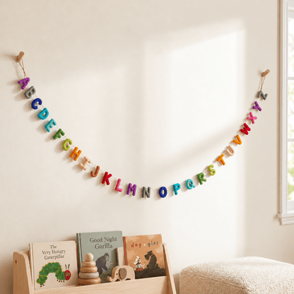 Colorful felt alphabet garland displayed in a bright, neutral children's room, styled with wooden toys and picture books, including dog+girl by Maria Murillo.