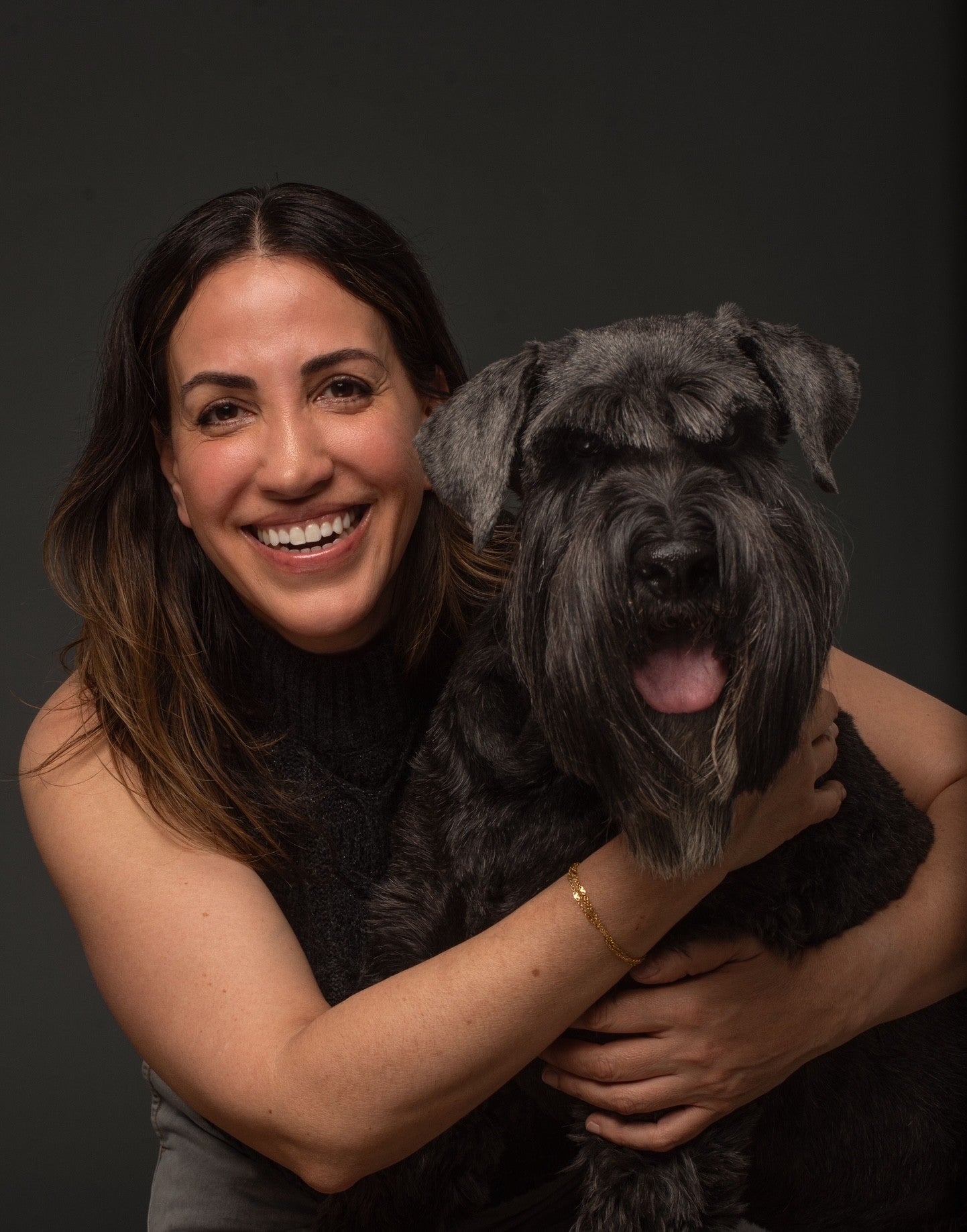Woman holding a black standard schnauzer dog against a dark background.